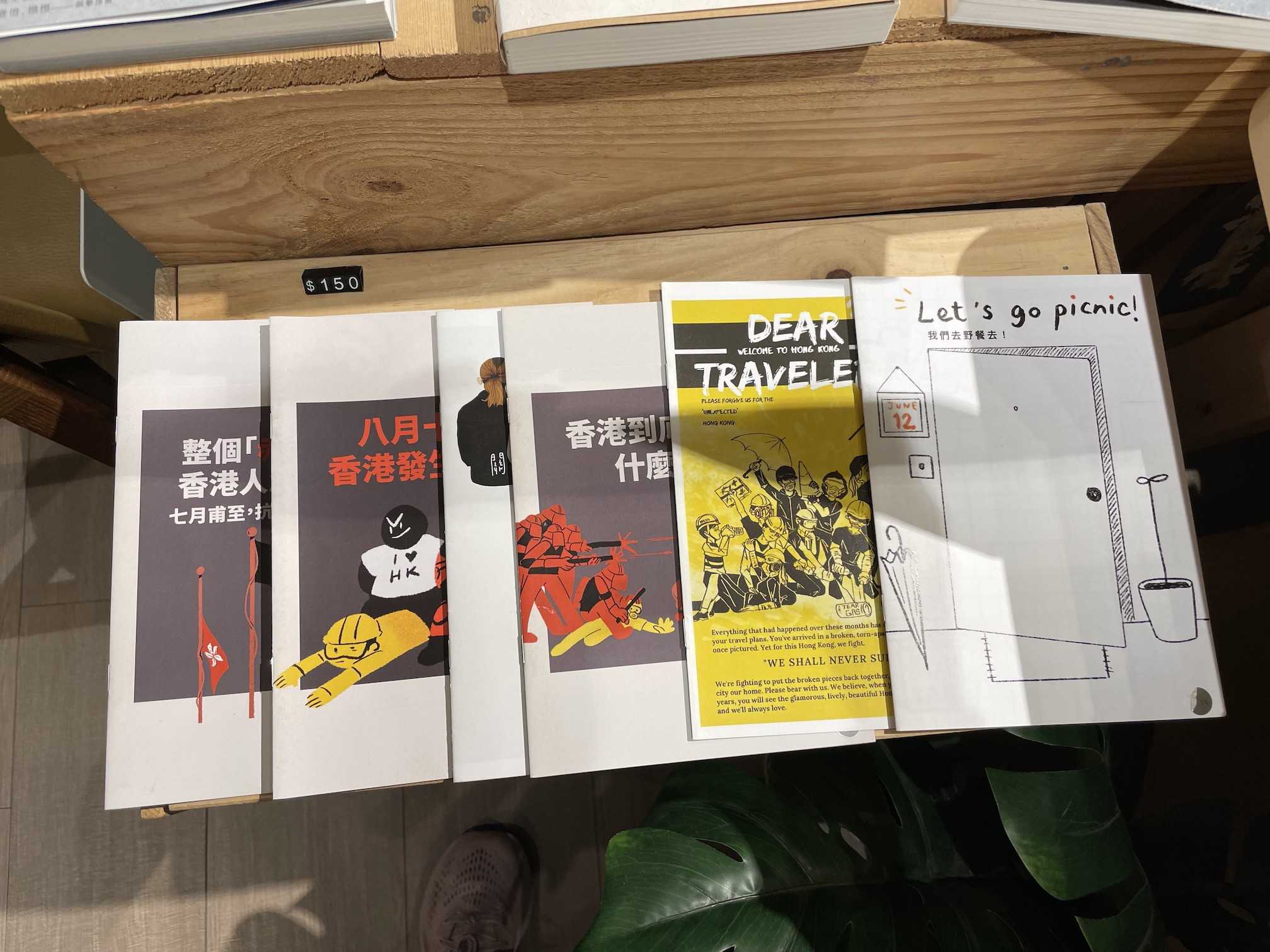 An assortment of six handmade magazines or zines with various titles like Let’s go picnic! and Dear Traveler: Welcome to Hong Kong are laid out on a wooden table. 